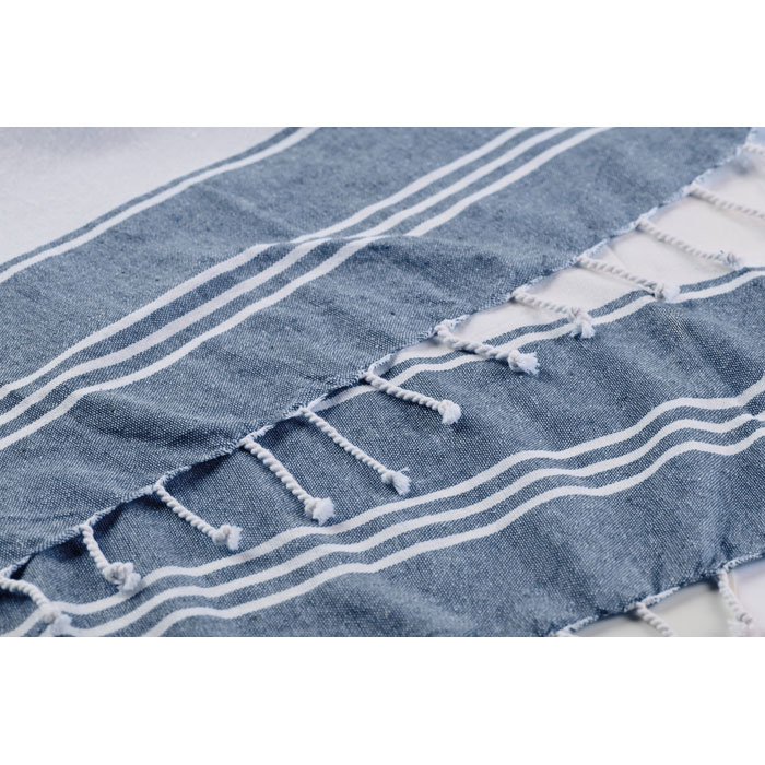 Set de playa azul HUMMUM compuesto por toalla fouta enrollada y bolsa tote de rayas con flecos.