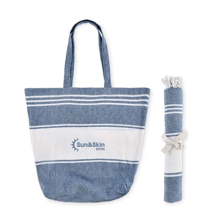 Set de playa azul HUMMUM compuesto por toalla fouta enrollada y bolsa tote de rayas con flecos.