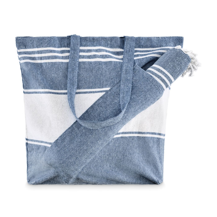 Set de playa azul HUMMUM compuesto por toalla fouta enrollada y bolsa tote de rayas con flecos.